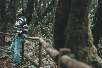 Serene happy tourist man standing and enjoying in outdoor forest park with foliage and trees around in the woods. Casual male mature admiring environment park outdoors in leisure activity adventure