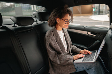 Executive woman manager working on laptop sitting car leather backseat on the way to office
