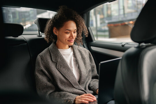 Cheerful businesswoman accountant working on laptop sitting car backseat on the way to office
