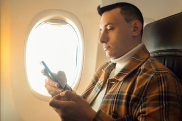 A man in a half-empty plane with a phone. Guy traveler looking at smartphone.