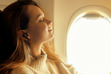 A girl in headphones is flying in an airplane and listening to music or podcast, audiobooks offline