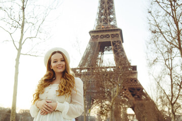 Beautiful blonde in Paris with the Eiffel Tower in the background in a beret and white dress. The woman is laughing and smiling, the girl is on a trip to France