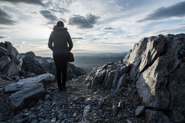 A woman stands with her back on the edge of the cliff. Rocky mountain at sunset.