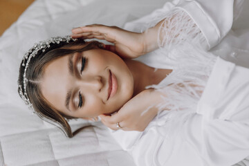 Morning of bride before the wedding. Beautiful young woman with long veil in a white robe. Natural beauty and professional make-up.Girl in white lace boudoir dress.