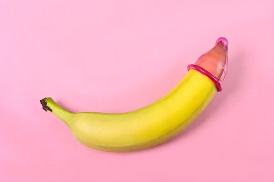 Condom on banana with pink background.. Concept of sexual protection.