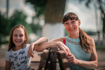 Fototapeta premium A young beautiful dark-haired mother is resting in a summer park with her young daughter.