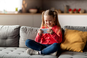 Gadgets For Kids. Cute Little Girl Relaxing With Smartphone At Home