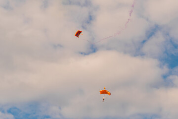 Two skydivers, parachutists flying with parachute against cloudy sky with white clouds at Air Show. Parachuting sport, extreme and leisure activity concept