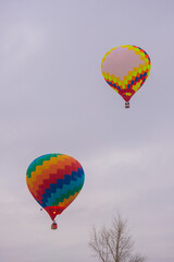 Two colorful hot air balloons flying against grey sky at Winter aerostat festival. Freedom, sport, aircraft concept