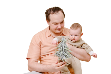 A man father and a boy son play with a small Christmas tree on the sofa in the home living room, isolated on a white background. Kid aged six months