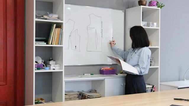 a young fashion designer girl draws on a blackboard a pattern of a dress for sewing clothes in a sewing studio