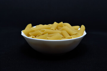 Wheat pasta in a white bowl on a black background. Dry pasta.