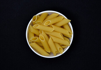 Wheat pasta in a white bowl on a black background. Dry pasta.