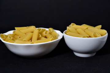 Wheat pasta in a white bowl on a black background. Dry pasta.