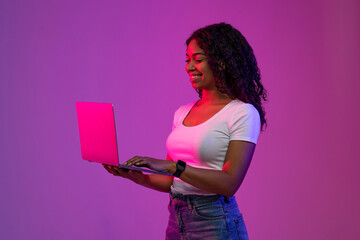 Black Woman Using Laptop While Standing In Neon Light Over Purple Background