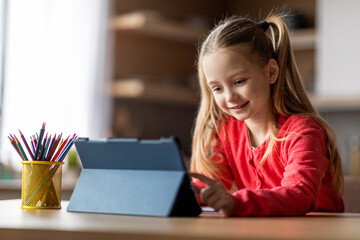 Cute Preteen Girl Using Digital Tablet While Sitting At Desk At Home