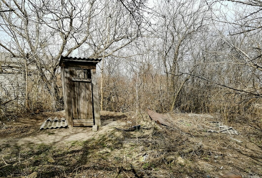 Outdoor WC. Wooden toilet booth outside. Toilet in the yard of the house. A wooden toilet is falling apart.