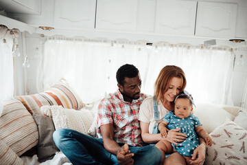 Portrait of candid happy interracial family with swarthy daughter sitting together on rv bed at day