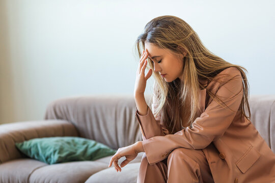 Mentally burnt out and completely devastated - young woman sits on the couch with her head in her hands.