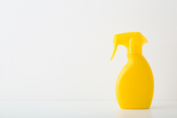 Yellow spray bottle of sunscreen or cleaning detergent on white table at light gray wall...
