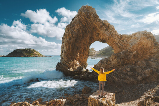 Tourist woman raised hands enjoying rocky arch in the sea view outdoor Travel in Greece, Rhodes island summer trip active vacations healthy lifestyle eco tourism