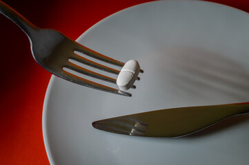 fork holding up a medicine pill on a red background - concept for eating problems, medicine abuse, chemical feeding, health problems