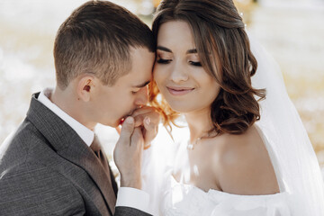 elegant beautiful couple. Hugs on each other. The groom kisses her hand. She lovingly leaned against him. Gorgeous light adds a romantic atmosphere.