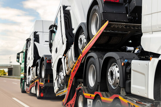 Back view of semi-trailer flatbed vehicle deliverying many new electric trucks sale automotive dealer from factory plant on highway interstate road. New business cargo transport fleet export import