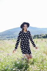 a woman in a hat walks in a field with daisies in nature