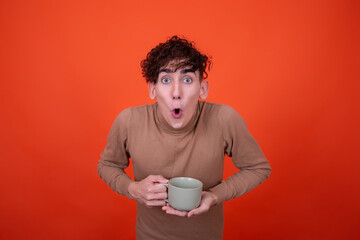 Funny young guy with a cup of hot coffee. Orange background.