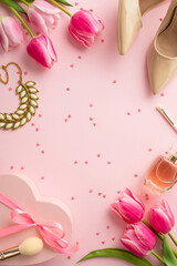 Women's Day concept. Top view vertical photo of pink tulips heart shaped present box beige shoes cosmetic brushes perfume necklace and sprinkles on isolated pastel pink background with blank space
