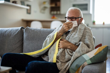 Fototapeta premium Sick and depressed older man is having high temperature and using handkerchiefs in the bed, trying to override the sickness. Senior man is fighting with the sickness and feeling desperate.
