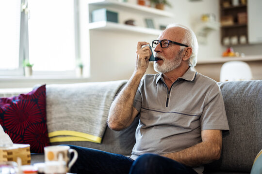 Senior man inhaling asthmatic cure at home. Man is living life with chronic illness everyday and overcoming challenges with It. Older man having an asthma attack due to his allergies.
