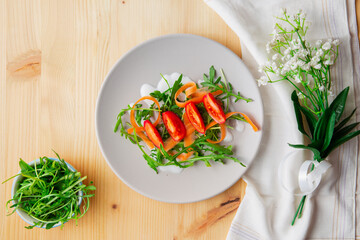 Top view of rocket salad with tomatoes, carrots and yogurt sauce on a grey plate, with flowers and...