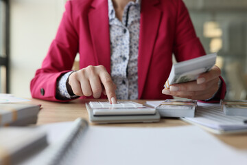 Fototapeta premium Female accountant sits at her desk and counts money with calculator.