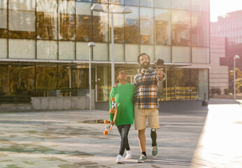 Obraz premium couple bloggers in the city- multiracial people with smart phone and skateboard. man with amputated leg wears prosthesis