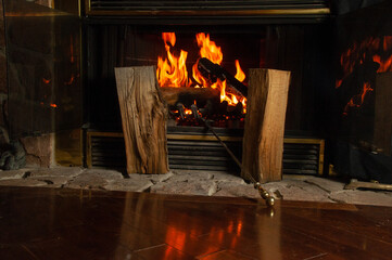 A fire in a home fireplace reflects off the hardwood. Two logs and the poker sit in front of the fire