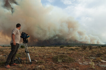 Un cámara de televisión graba un gran incendio en el horizonte.