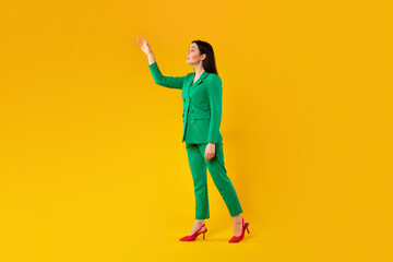 Fototapeta na wymiar Stylish young lady touching invisible object, showing and advertising something, standing over yellow background