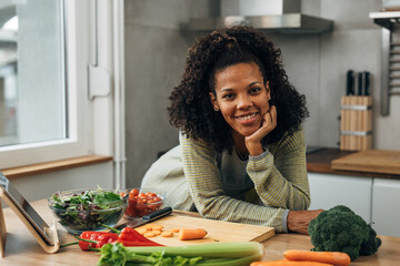 Front view of a mixed race woman leaning on a kitchen table with vegetables on it
