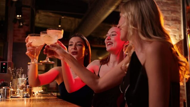 Girlish party. hree beautiful young girls meeting together at restaurant, bar, drinking cocktails, talking and having fun. Friendship, meeting, fun, clubbing, party and celebration concept