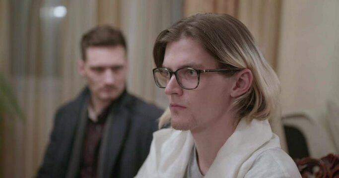 Two men sitting in a room in silence. Stock. Man with dyed long blond hair wearing glasses.