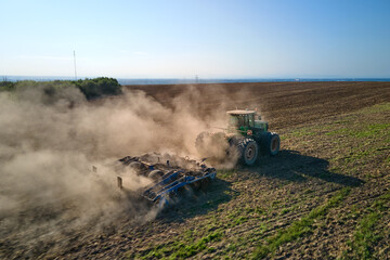 Aerial view of tractor plowing agriculural farm field preparing soil for seeding in summer