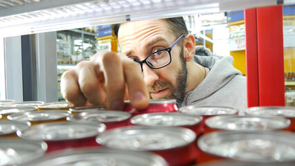 Close-up of the face of a bearded man with glasses taking a can from a store fridge