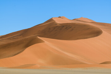 Rolling red desert dune in Deadvlei, white sand in foreground, blue cloudless sky