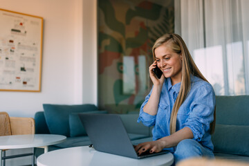 Smiling girl using a laptop while talking to someone over the phone.