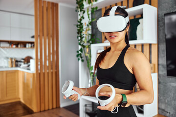 A pretty Asian female using a VR headset and holding a controller while doing a home workout.