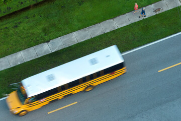 Top view of classical american yellow school bus driving on rural town street for picking up kids...
