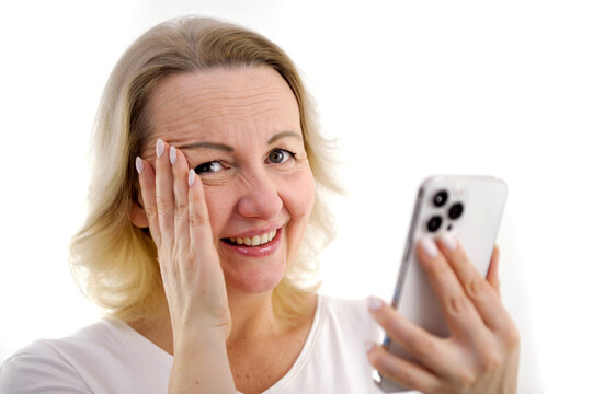 embarrassment inconvenience experiences self-blame woman smiles at ashamed she looks at the camera shy covered her eyes with her hand in her hands white phone gentle smile reaction to dirty joke