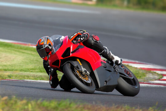 a motorcycle rider on a red sport bike riding through a corner at high speed, leaning the bike, dragging a knee and an elbow